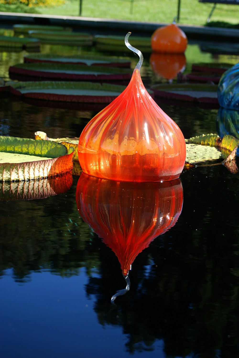 a red glass vase sitting on top of a pond