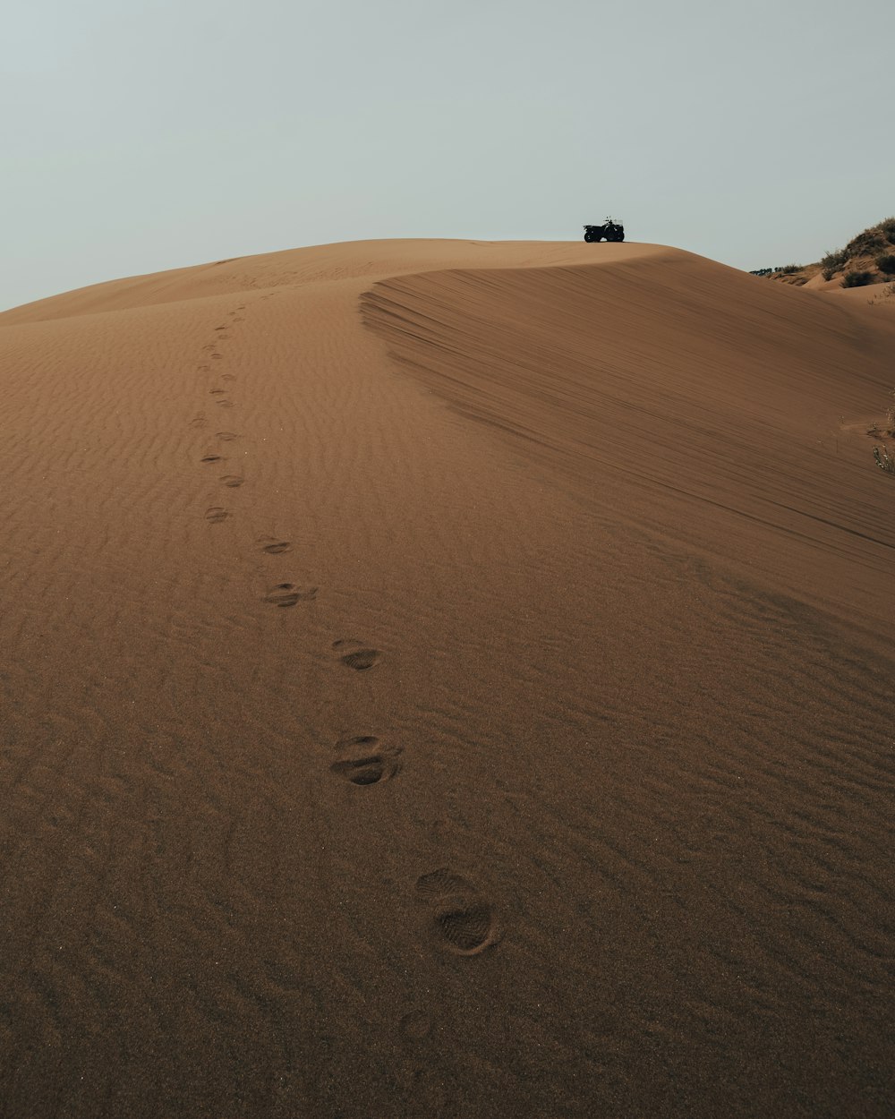 a jeep driving down a sandy hill with footprints in the sand