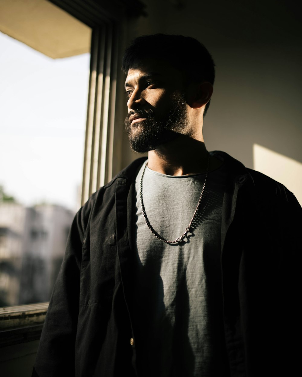 a man standing in front of a window with a necklace on