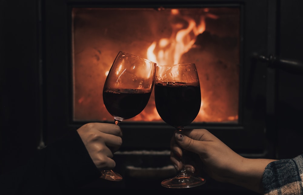two people holding wine glasses in front of a fireplace
