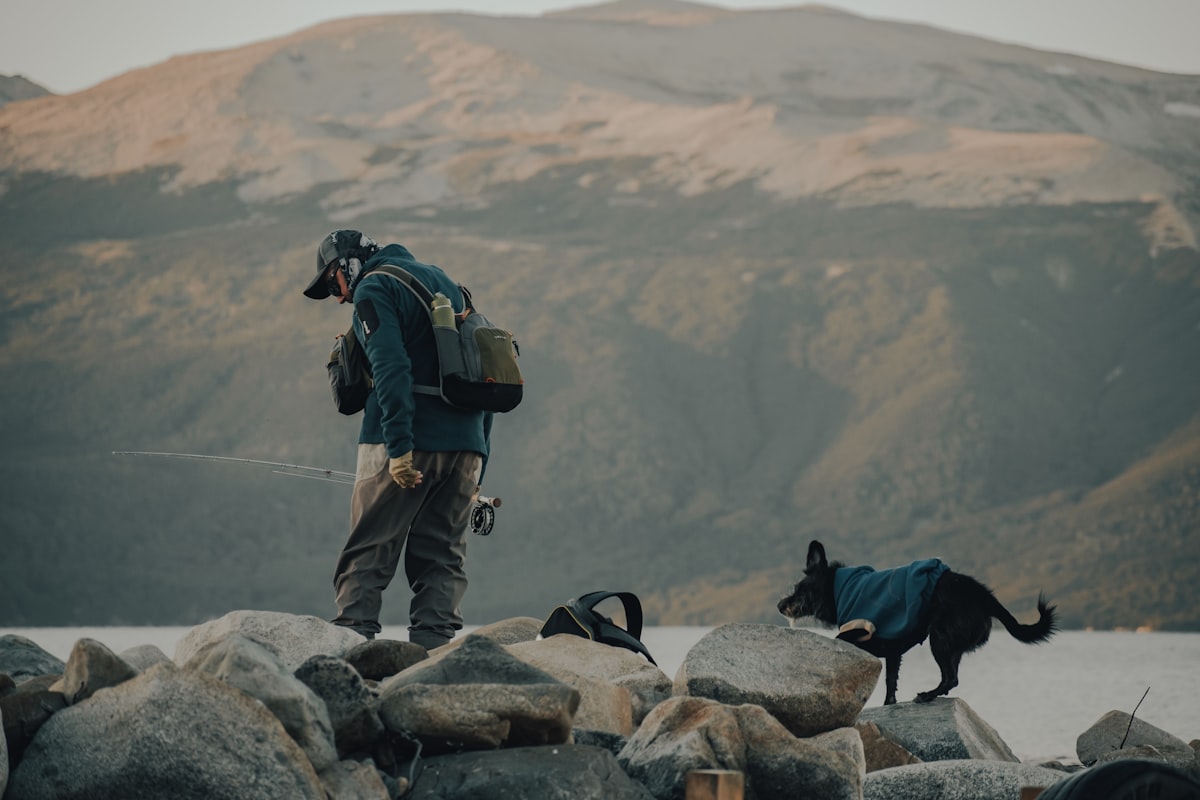 A man with a backpack and a dog standing on a rocky shore