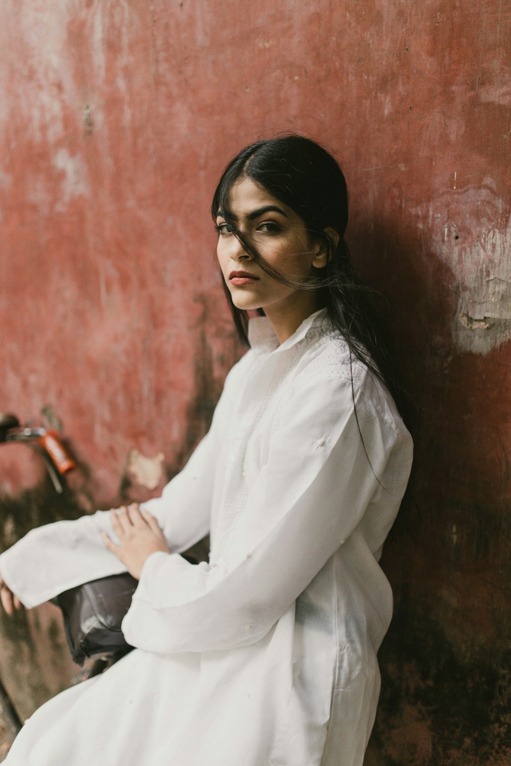 a woman in a white dress leaning against a red wall