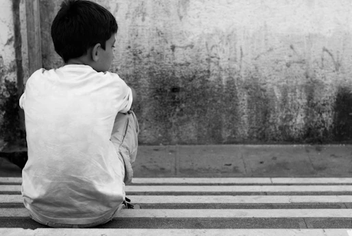 a young boy sitting on the side of a street