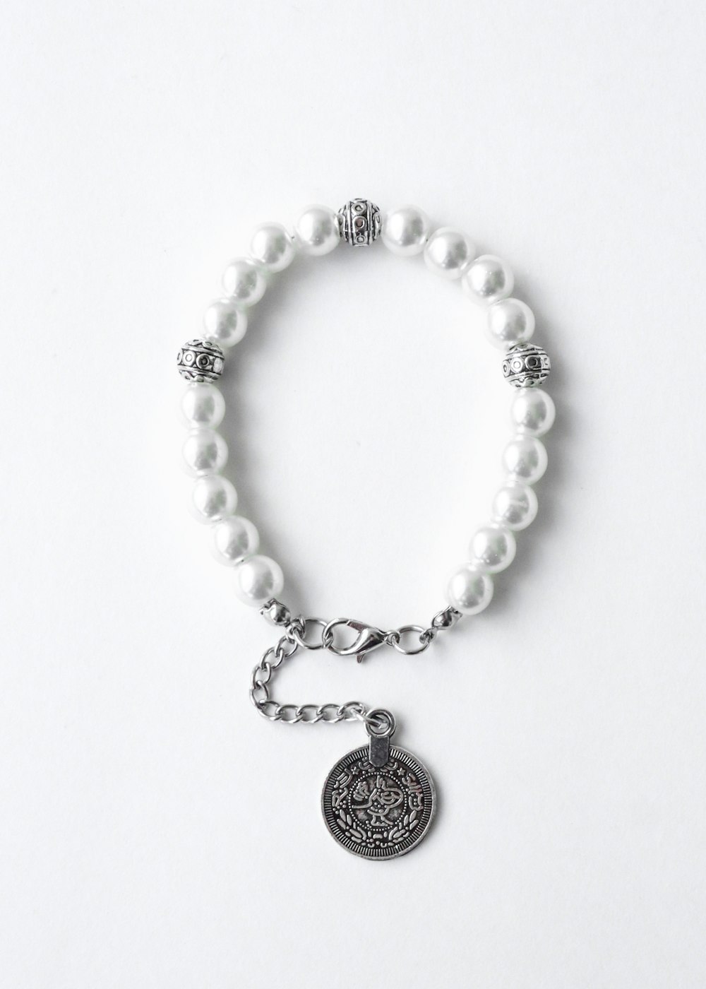 a white beaded bracelet with a silver charm