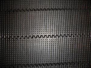 A close-up view of a metal or plastic grate with evenly spaced rectangular slits forming a repetitive pattern, creating a sense of depth and symmetry.