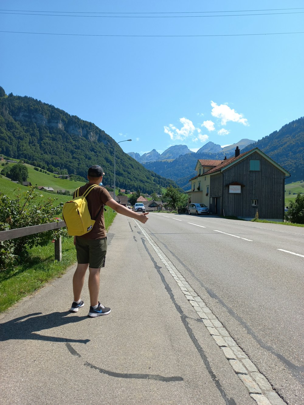 Un hombre con una mochila amarilla parado al costado de una carretera