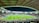 A large football stadium filled with spectators. The field is brightly lit, and two teams are positioned on the pitch. The stadium is covered, with a visible roof structure and stands filled with fans. Scoreboards are visible displaying game information.