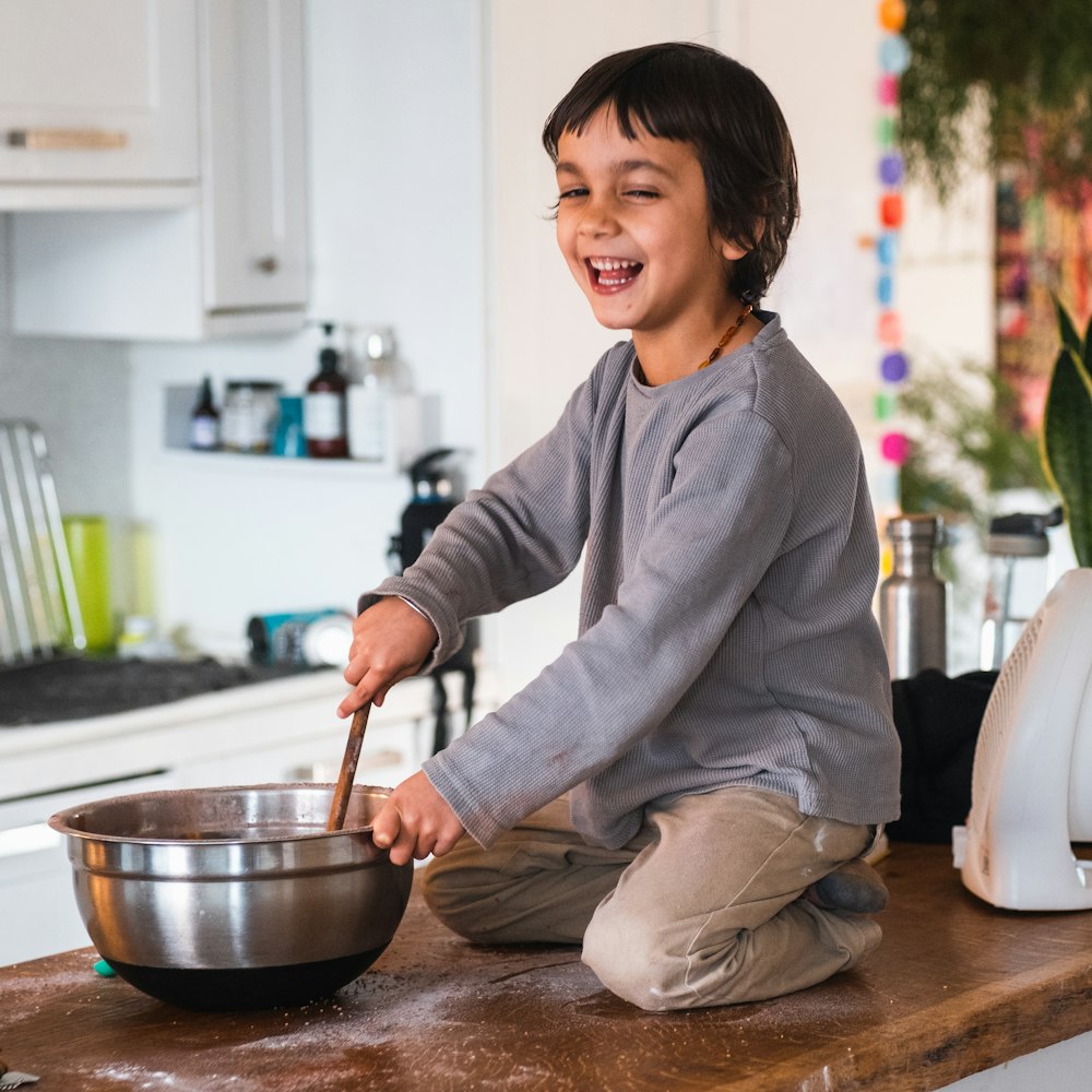 a young boy sitting on a kitchen counter stirring a bowl