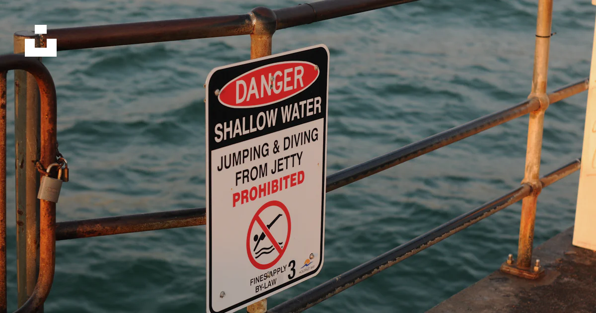 A warning sign on a railing near a body of water photo – Free Sign ...