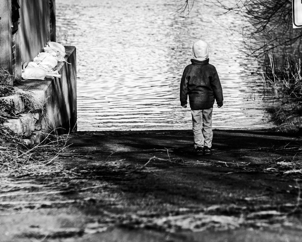 a black and white photo of a person walking towards a body of water