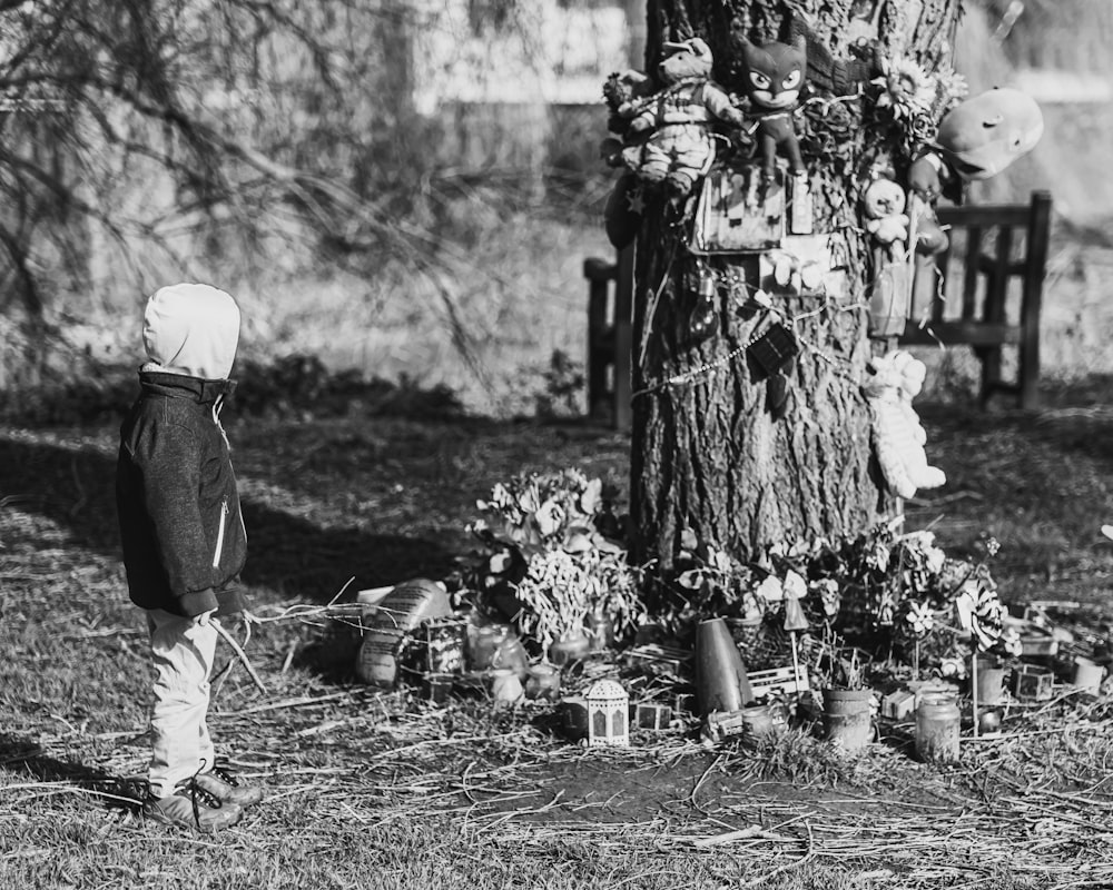 a little boy standing in front of a tree