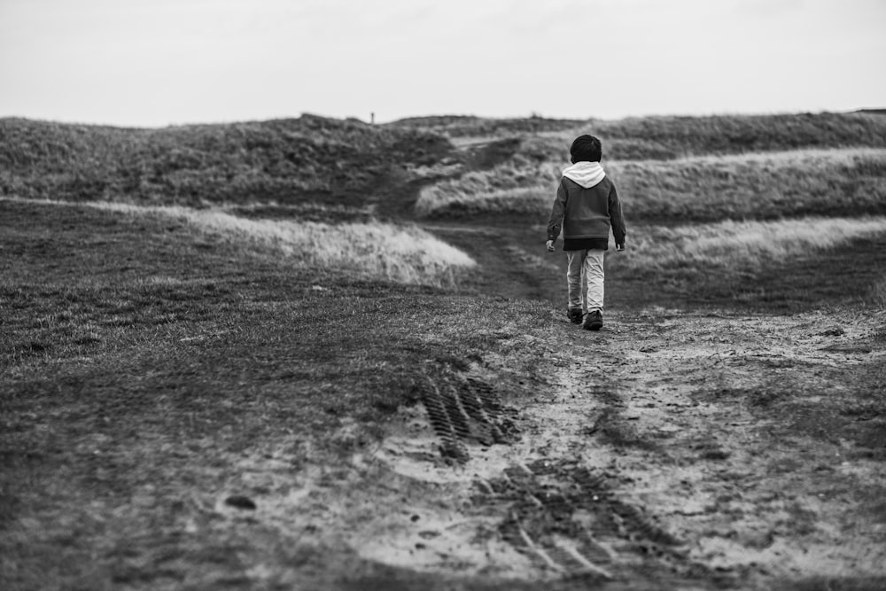 a black and white photo of a person walking on a dirt path