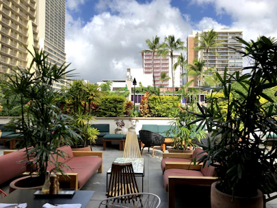An elegant outdoor BBQ area with modern furniture and lush tropical plants.