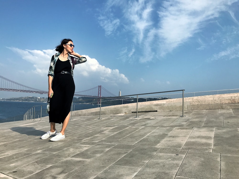 a woman in a black dress is standing on a pier