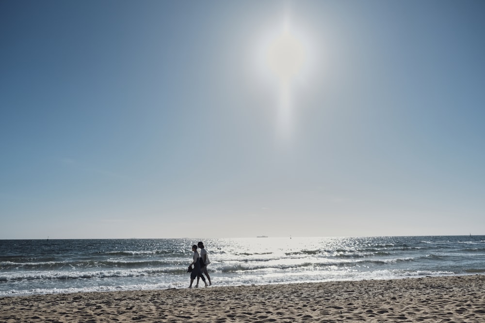 a couple of people standing on top of a sandy beach