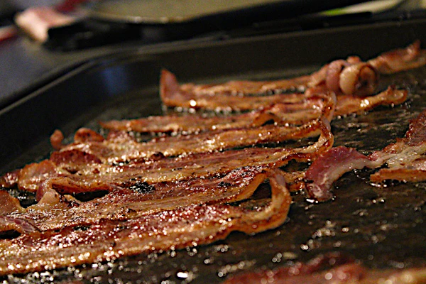 Close-up of thick-cut smoked bacon sizzling on a cast iron skillet, with rich smoky textures and golden edges.