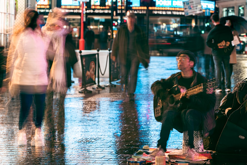 a man sitting on a sidewalk playing a guitar