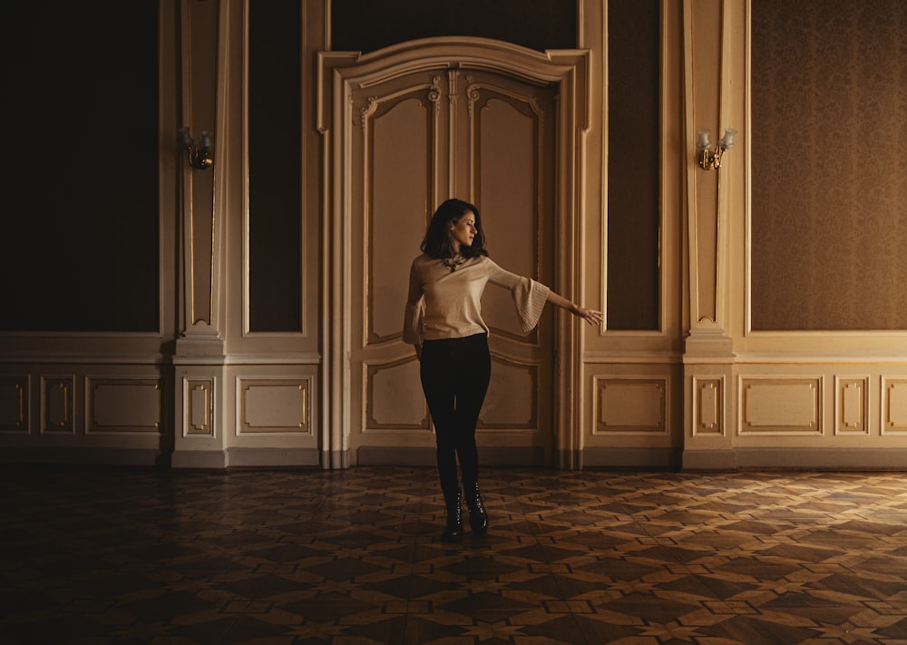 a woman in a white sweater and black pants standing in a room
