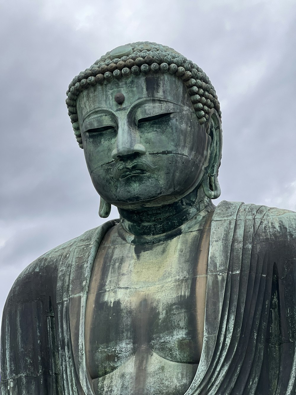 Una gran estatua de un Buda con un cielo nublado en el fondo