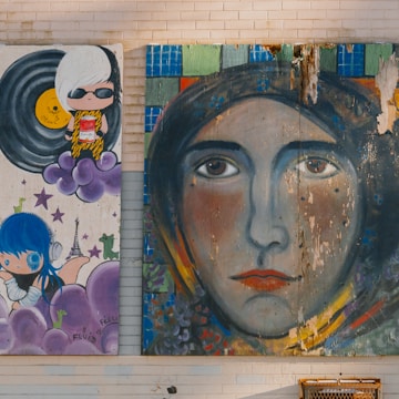 A wall is adorned with two vibrant murals. The left painting depicts two cartoon-like figures with colorful, whimsical elements including vinyl records, purple clouds, and the Eiffel Tower in the background. The right mural features a large, expressive face with eyes that gaze directly outward, surrounded by a patchwork of colors and textures.