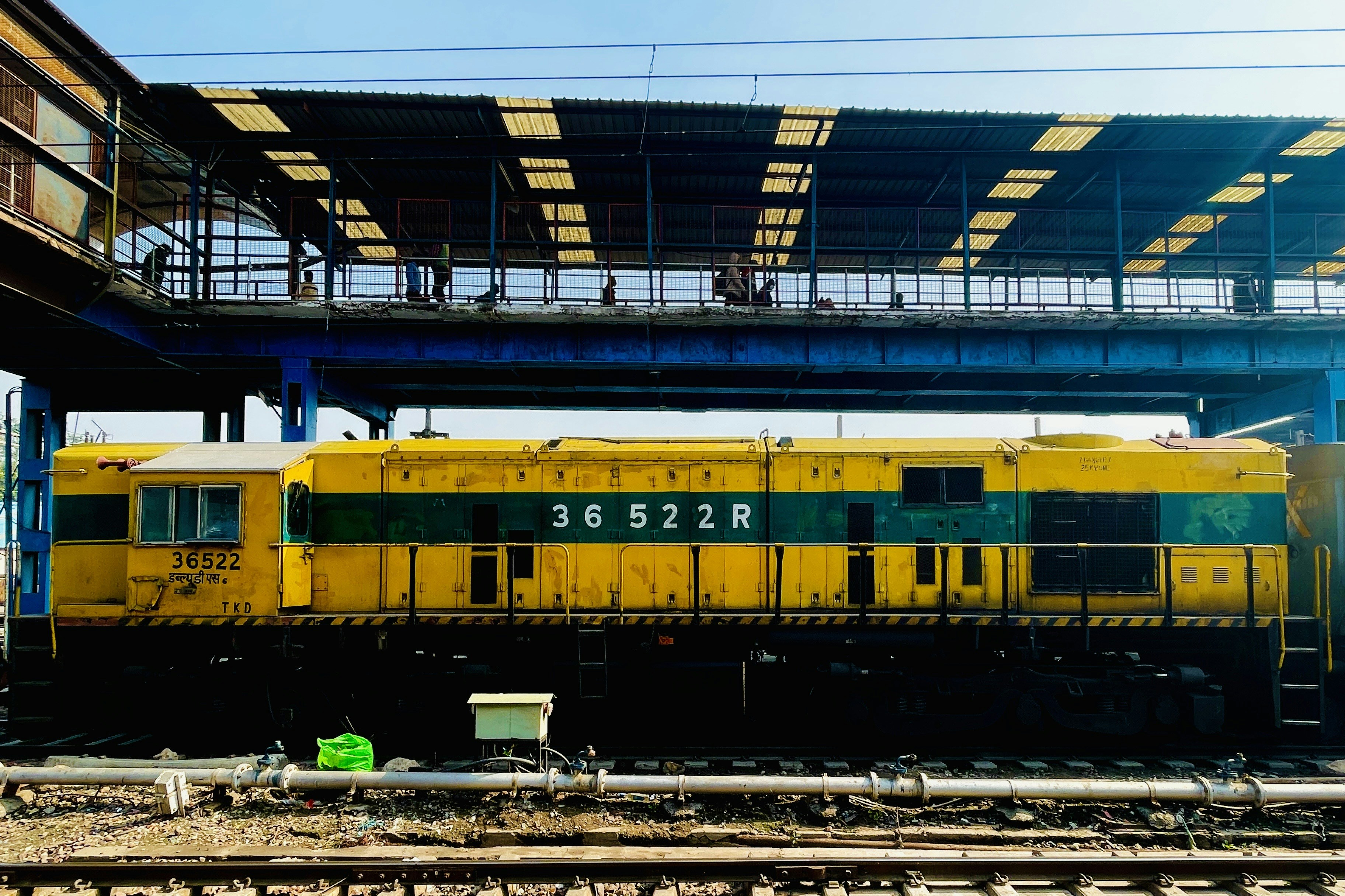 a yellow and green train sitting under a bridge