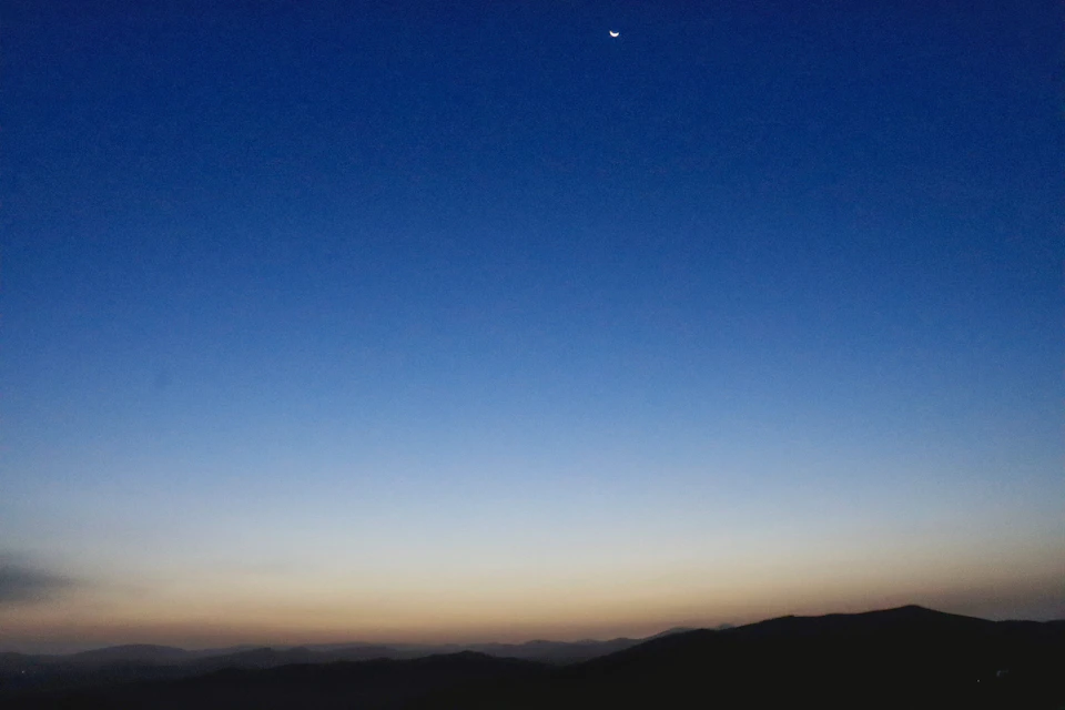 Serene night sky features large bright moon partially obscured by clouds and crescent shape