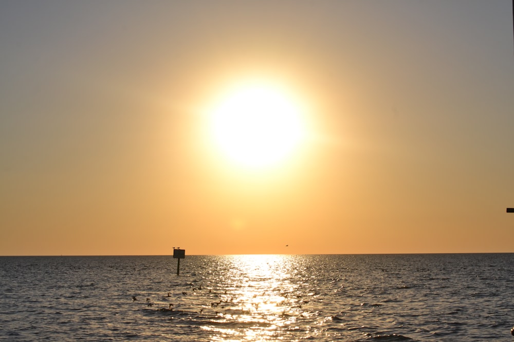 the sun is setting over the ocean with a boat in the water