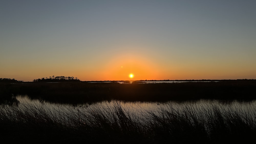 the sun is setting over a marshy area