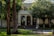 A building facade with the words 'Fuller Theological Seminary' above a set of arched doors, surrounded by lush green trees and neatly manicured lawns. The entrance is accessed by a short staircase, with a bench and pathway leading to it.