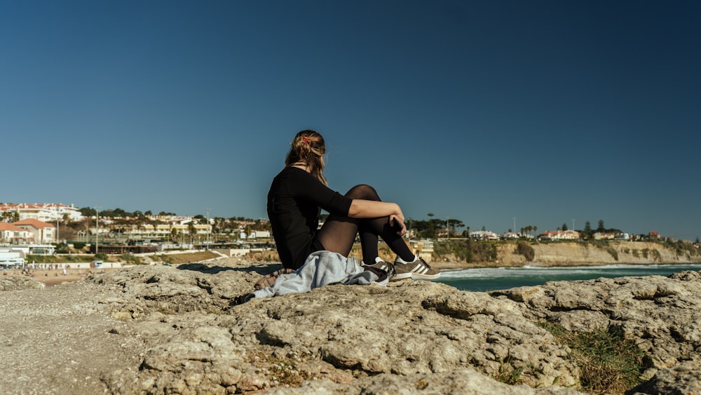 a woman sitting on top of a rock next to the ocean