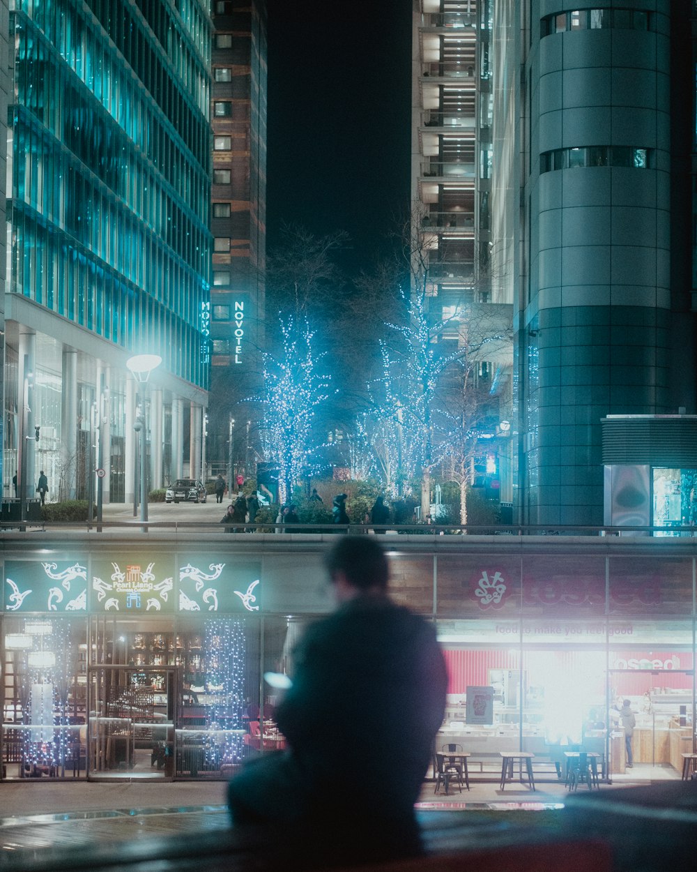 a man sitting on a bench in a city at night