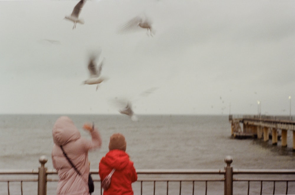 a couple of kids standing next to each other near a body of water