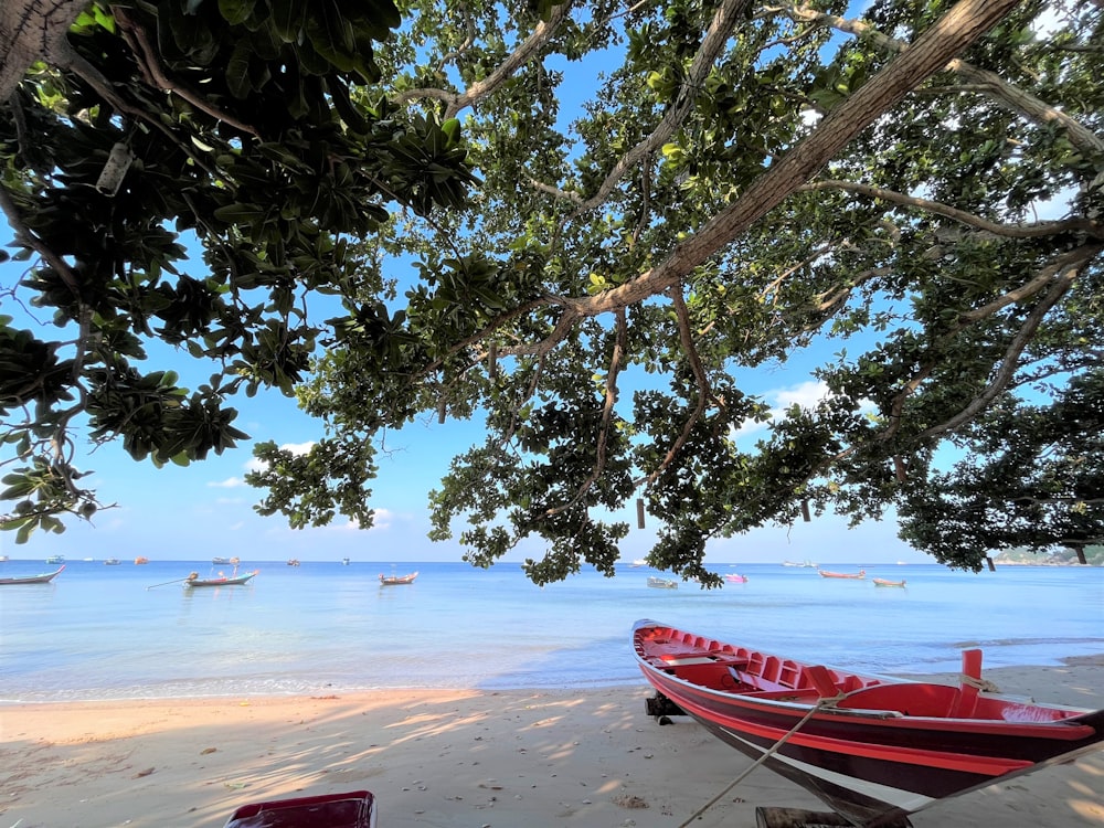 a red boat sitting on top of a sandy beach