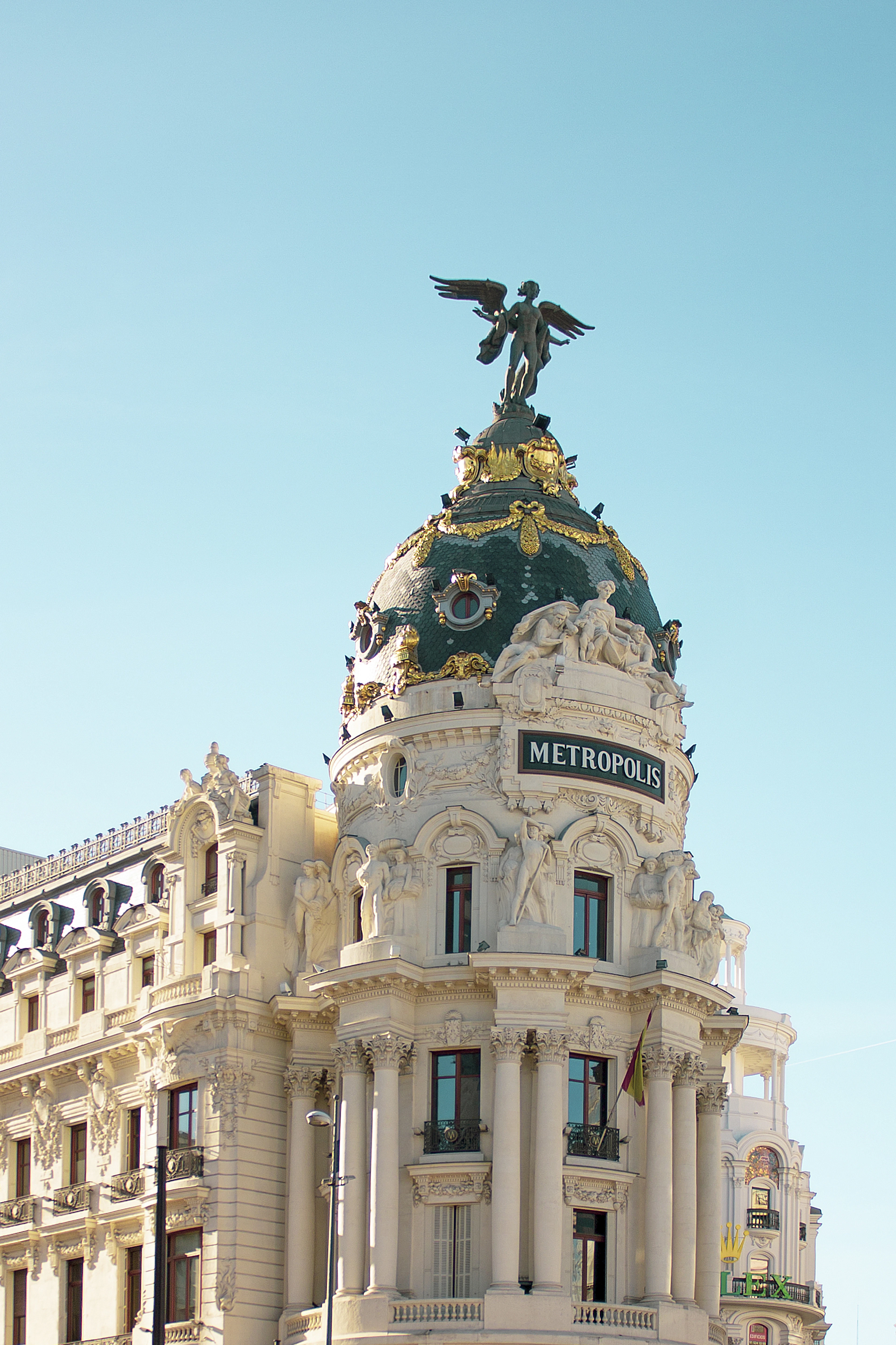 The Metropolis Building's gilded winged-victory statue and green dome catch late sunlight.