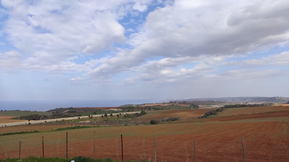 a field with a fence and a road in the distance