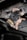 A gloved hand is wiping or cleaning a mechanical part, possibly an engine or a machine, using a crumpled cloth or paper. The setting appears industrial or mechanical, with a focus on maintenance.