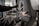 A person wearing protective gloves is handling a car tire. The tire is mounted on a wheel with a metallic rim, and the scene appears to be in a workshop or garage environment, with equipment visible in the blurred background.