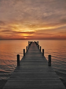 a long dock extending into the ocean at sunset