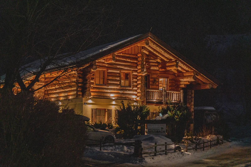 A warmly lit timber chalet glowing against the snow on a clear alpine night