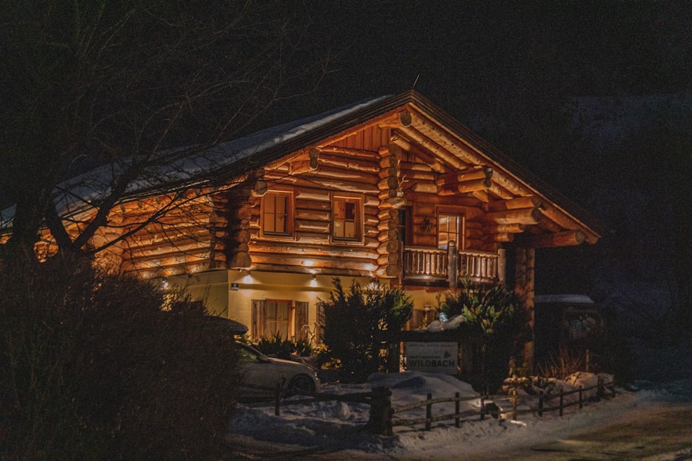 eine Blockhütte, die nachts im Schnee beleuchtet wird