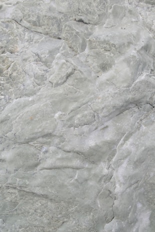 A close-up view of a textured stone surface with various shades of green. The surface features intricate patterns and natural formations, giving it a rugged and earthy appearance.