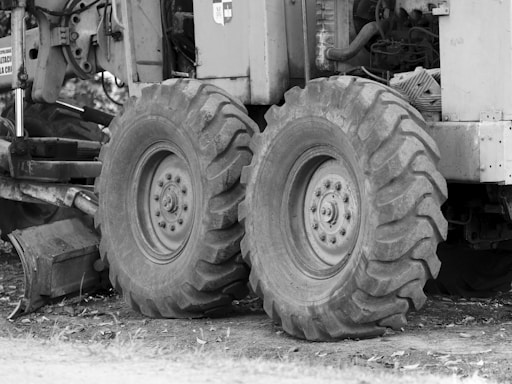 Large tractor tires attached to industrial machinery are positioned on rough terrain. There are visible mechanical components and metal parts surrounding the wheels.