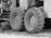 Large tractor tires attached to industrial machinery are positioned on rough terrain. There are visible mechanical components and metal parts surrounding the wheels.