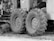 Large tractor tires attached to industrial machinery are positioned on rough terrain. There are visible mechanical components and metal parts surrounding the wheels.