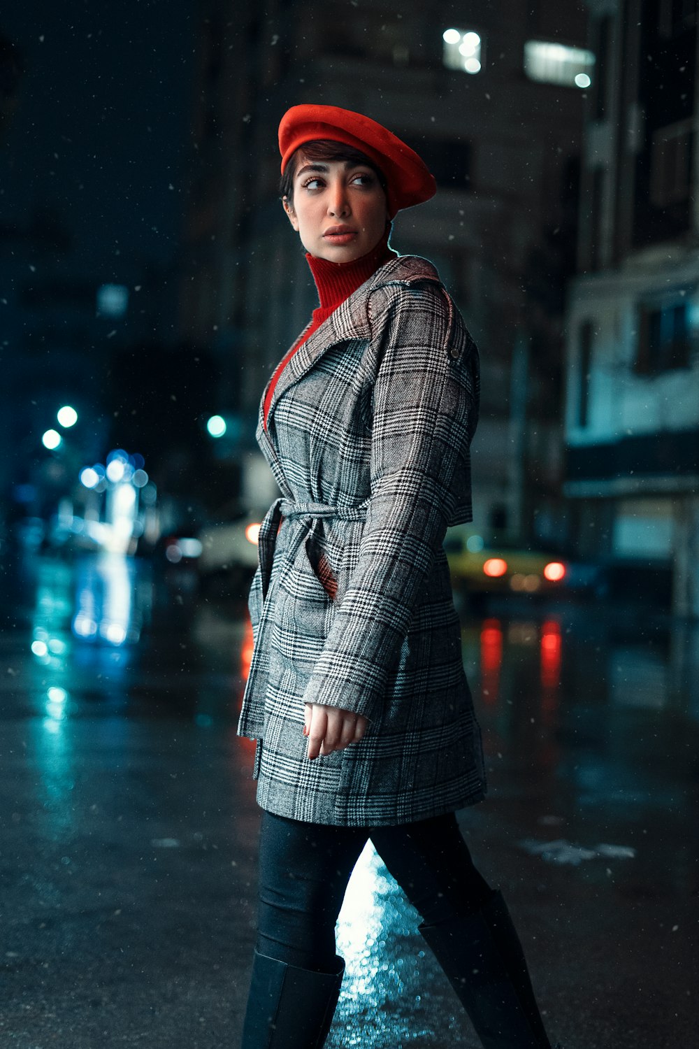 a woman in a plaid coat and red hat is walking in the rain