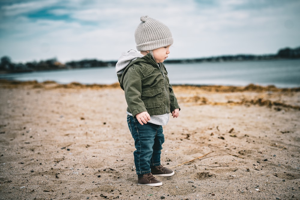 a young boy standing on a beach next to a body of water