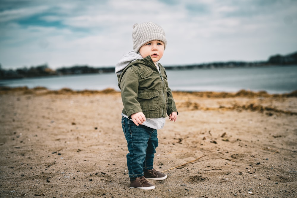 a little boy standing on a beach next to a body of water