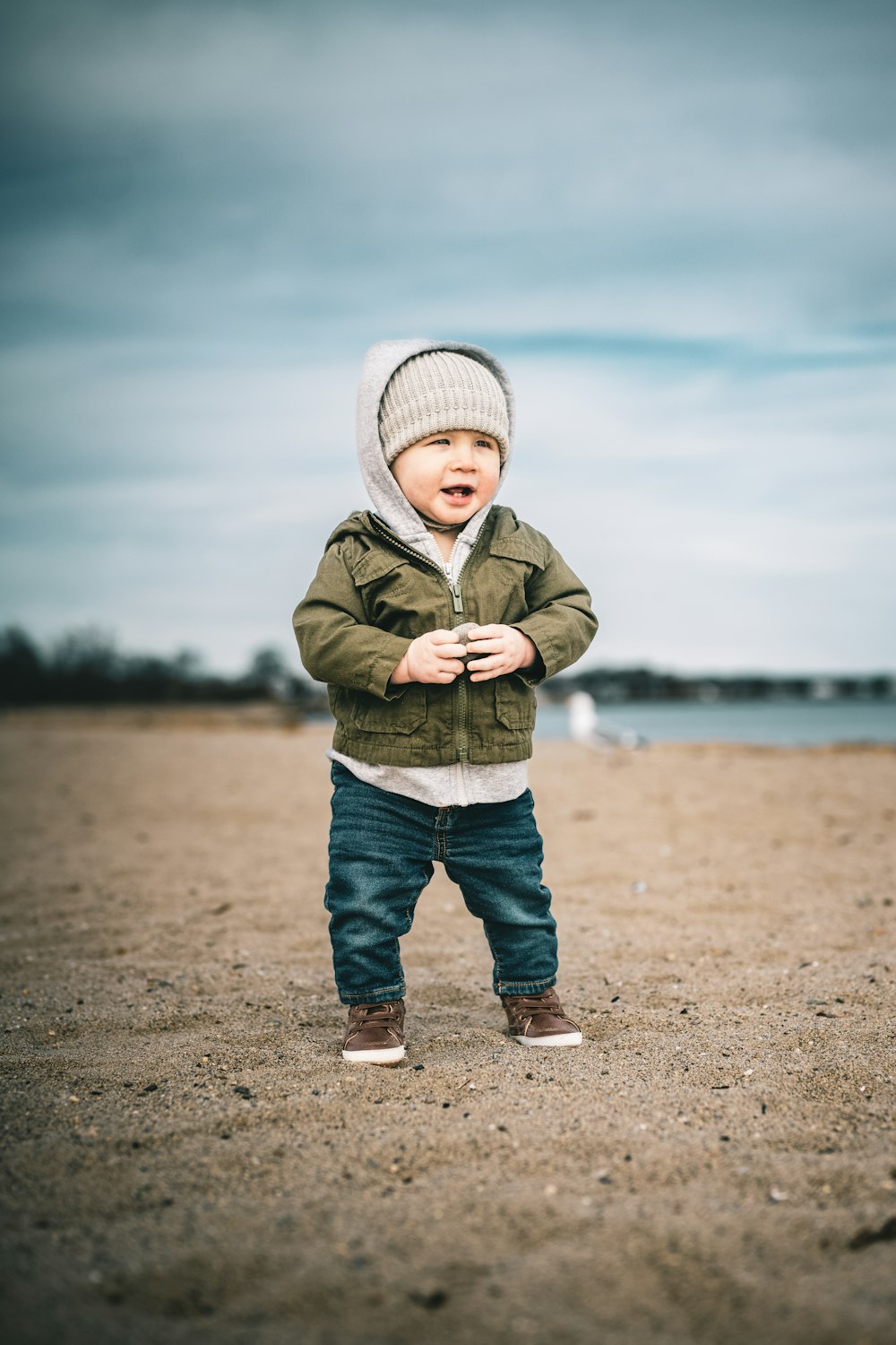 a toddler standing on a beach with a hat on