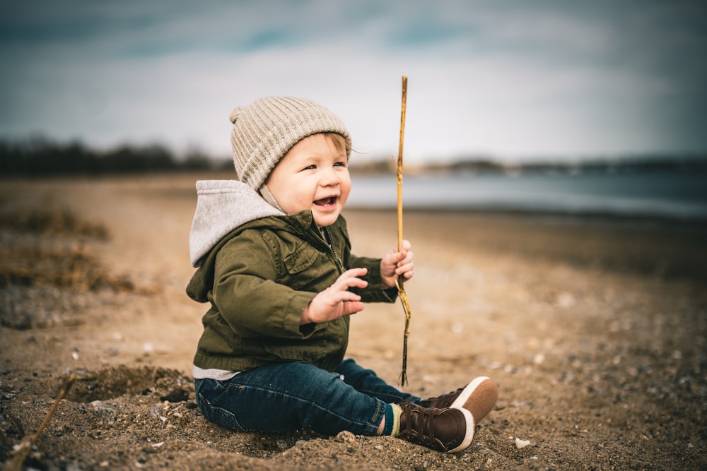 a baby sitting on a beach holding a stick