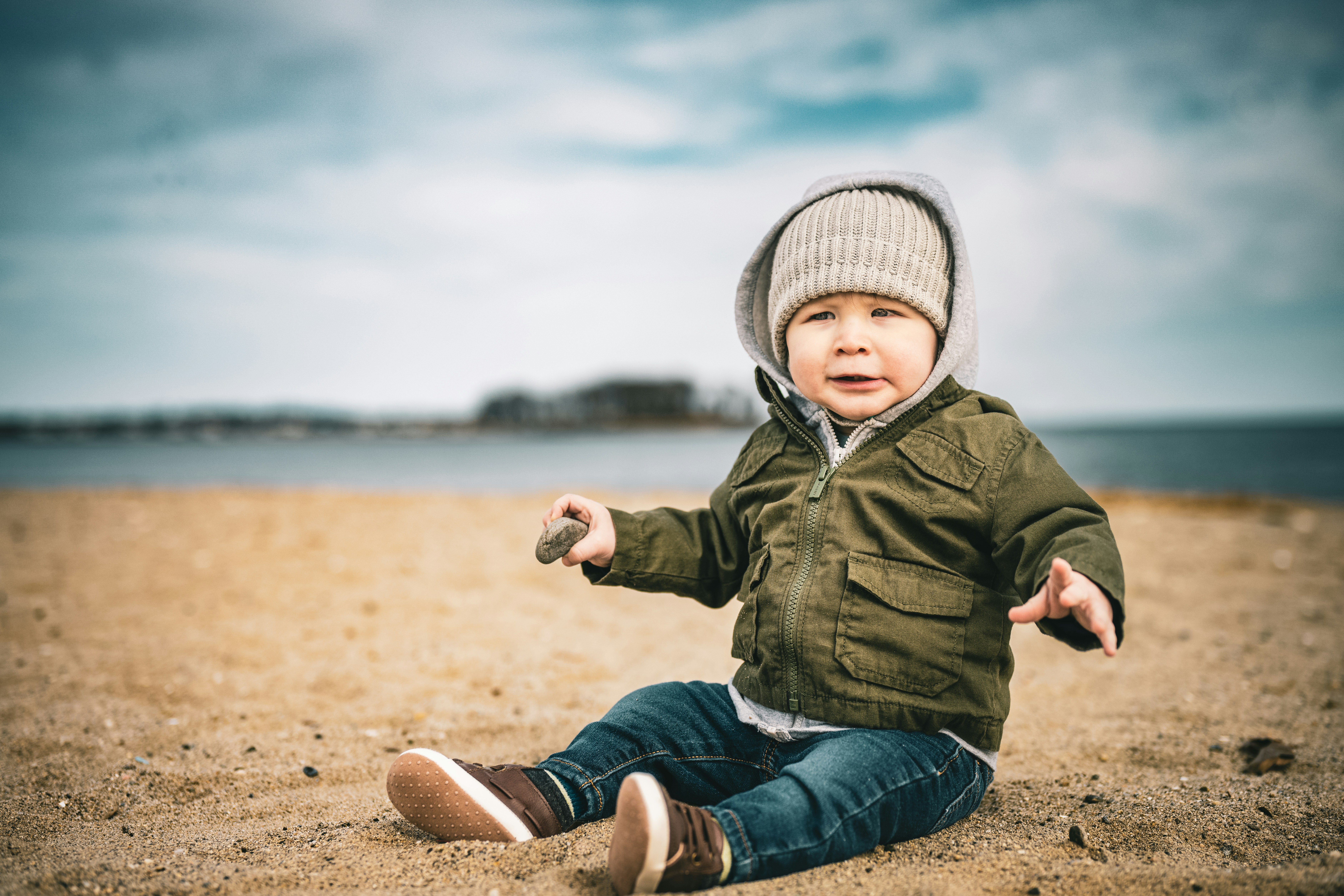 a little boy sitting on the beach with his hands out